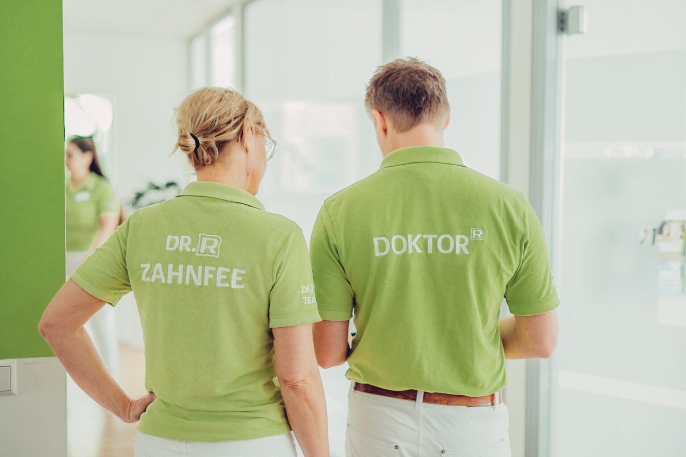 Zahnfee und Doktor der Praxis Dr. Rathgeber von hinten in ihren grünen Praxisshirts